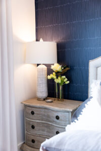 a night stand with a lamp against a blue wallpapered wall